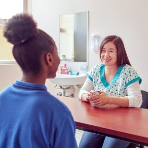 smiling speech therapist working with playing cards with black teenage secondary school student